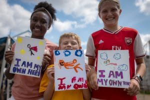 three children holding hand painted signs saying I am my own hero at camp mirage, Eras Tour Art Exploration Camp
