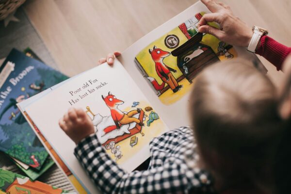 A child and adult reading an illustrated storybook together in a cozy setting. Babysitting Camp