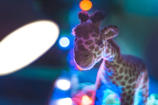 Animal Planet Camp a Close-up of a cute stuffed giraffe toy with colorful bokeh background lighting.